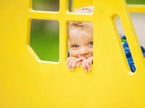 Young child playing peek-a-boo behind a large yellow window